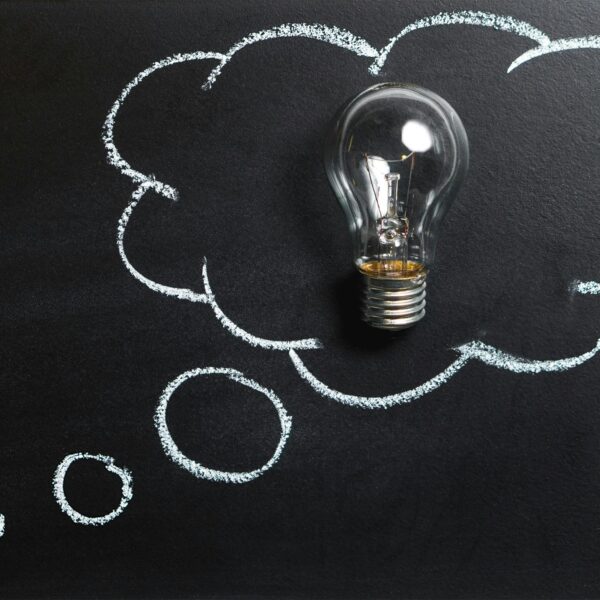 Light bulb laying on chalkboard with drawn thought bubble, symbolizing creative ideas.